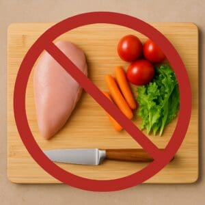 Raw chicken and fresh vegetables placed together on a cutting board with a no symbol overlay — warning about cross-contamination in home cooking.