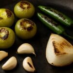 Tomatillos, serrano peppers, onion, and garlic roasting in a cast iron skillet.